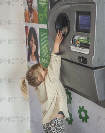 Blond girl, 5 years old, earns pocket money by recycling cans in recycling machine in Ystad, Skåne