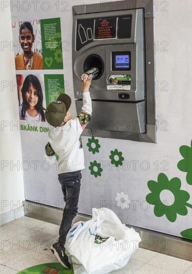 Boy, 7 years old, earns pocket money by recycling cans in recycling machine in Ystad, Skåne County,