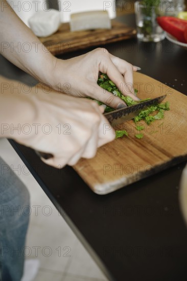Unrecognizable woman chopping cilantro on wooden cutting board