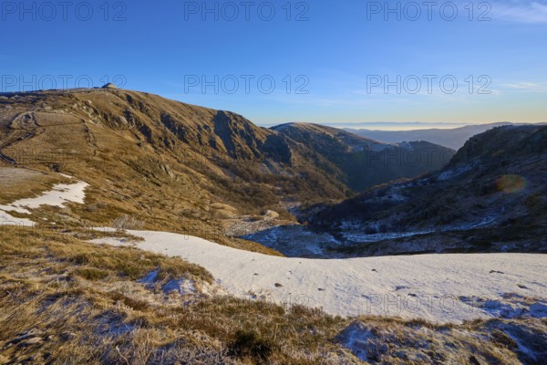 Extensive mountain landscape with snow and trail under clear sky in the morning sun, winter, Route