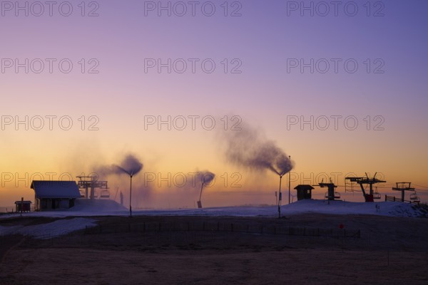 Snow cannons blow smoke under purple and orange evening sky, winter, Route de Cretes, Hohneck, La