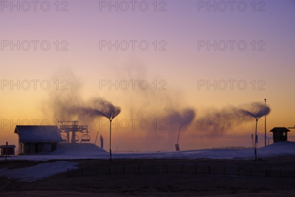 Under a dramatic sunset sky, snow cannons blow smoke across the empty hill, Winter, Route de