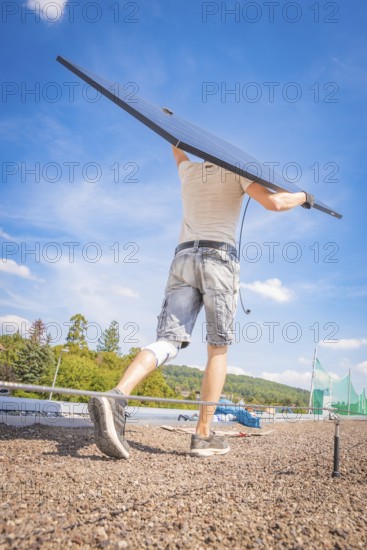 A worker lifts a solar module against the blue sky, new Park and Ride parking garage Calw Heumaden