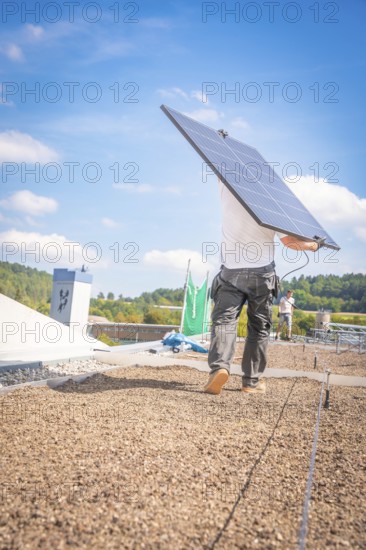 A worker carries a solar panel over the roof in sunny weather and blue skies, new park and ride