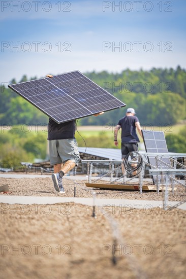 Workers install solar panels with cables in an open field under a blue sky, new park and ride