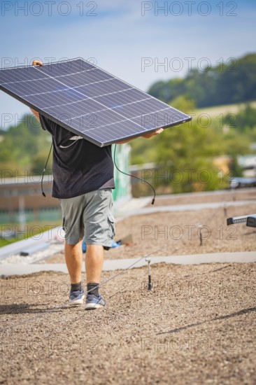 Man carrying solar panel on a gravel roof in front of a natural landscape, new park and ride