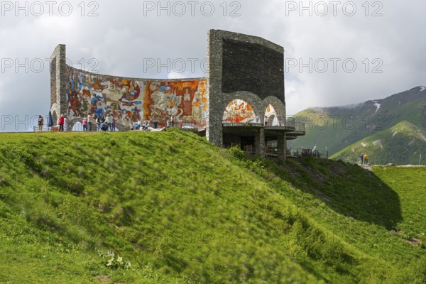 Grassy hill with painted wall, people enjoying the view, Georgian-Russian Friendship Memorial,