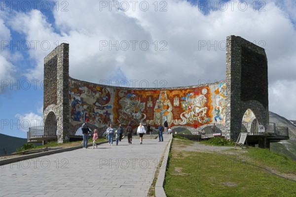 People look at a large wall painting on a curved stone wall, Georgian-Russian Friendship Memorial,