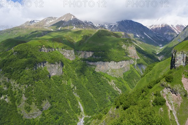 Green mountains with deep gorges under cloudy sky, mountainous landscape between Gudauri and Cross