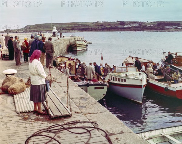 People boarding tour boats from the quayside in the harbour at Hugh Town, Isles of Scilly,