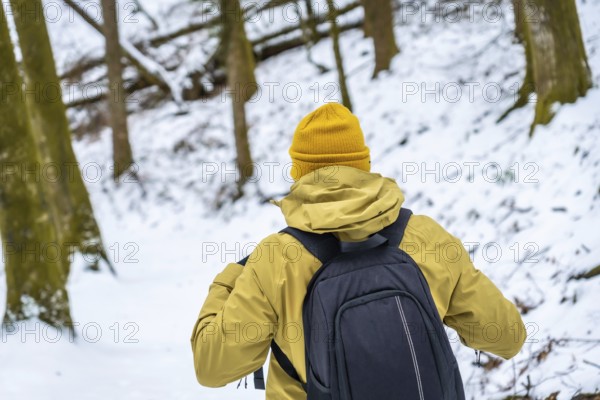 Hiker with backpack and yellow beanie navigating a snow covered forest, embracing the cold weather