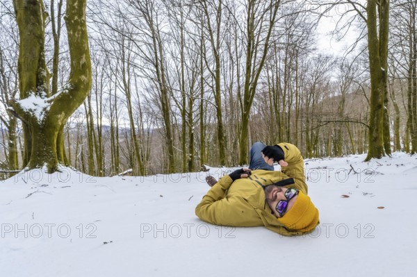 Man wearing a yellow winter jacket and hat, sunglasses, lying relaxed on the snow covered ground in