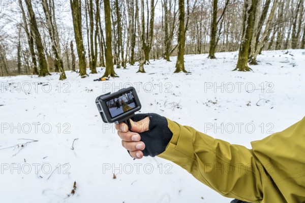 Person holding an action camera showing live footage while hiking through a snow covered forest,