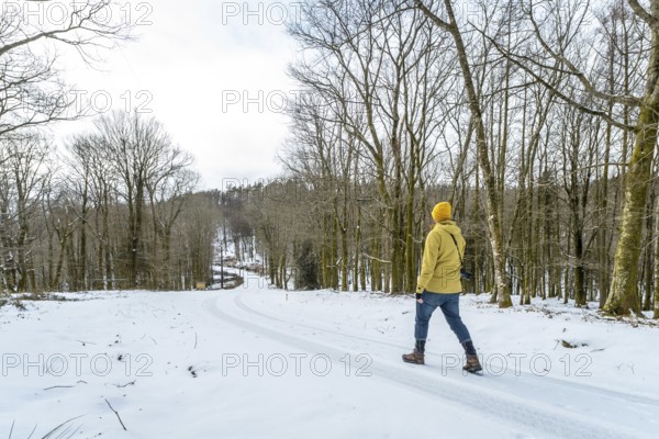 Person with yellow jacket and beanie beanie walking down a snow covered road winding through a bare