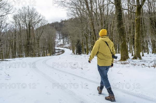 Man with camera backpack trekking a winding snowy path through a bare winter forest, enjoying