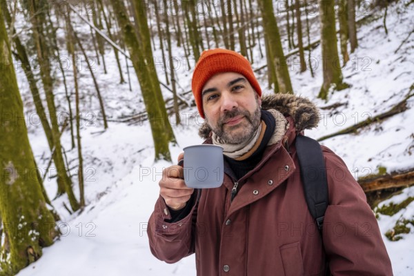 Man with an orange beanie and a winter coat holding a mug of a hot beverage, finding warmth and