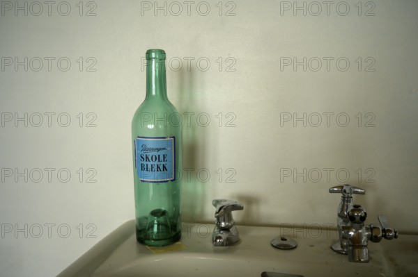 Green bottle with the Norwegian inscription Schukl ink a sink in front of a simple wall with retro