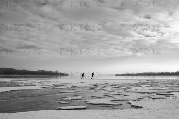 Two people walk across an icy water surface under a cloudy sky, black and white photography,