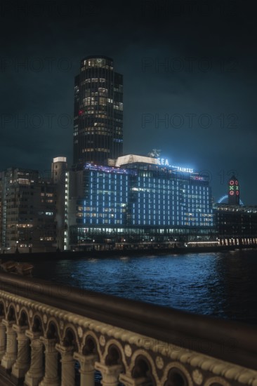 A towering, illuminated building on the riverbank at night against a dark sky, London, England,