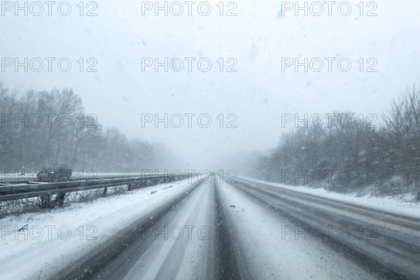 View through the windshield of a passenger car driving through light snowblowing on partly