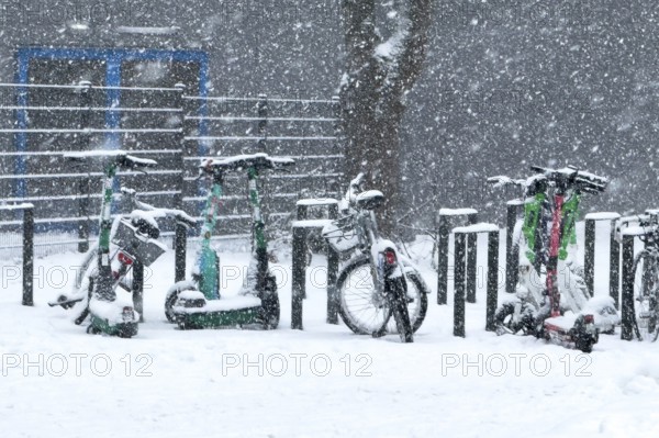 Tailored parked e-scooters and bicycles in winter during snowfall with snowflakes in the picture,