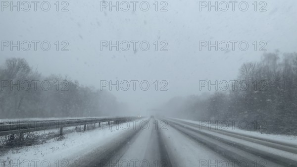 View through the windshield of a passenger car driving through light snow on an empty, partially