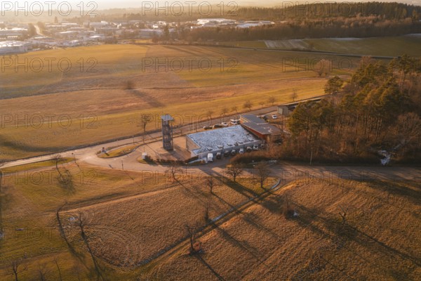 Aerial view of a landscape in evening light with fire station surrounded by fields and trees,