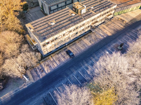 Building complex with empty parking spaces, surrounded by a winter tree landscape, MG4 electric