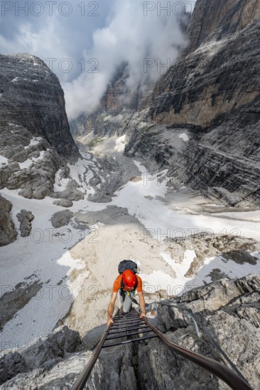 Mountaineer climbs a ladder in steep rocky terrain, Via Ferrata Oliva Detassis via ferrata, view of