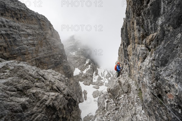Mountaineer climbs the Via Ferrata Oliva Detassis via ferrata, steep cliffs covered in clouds,