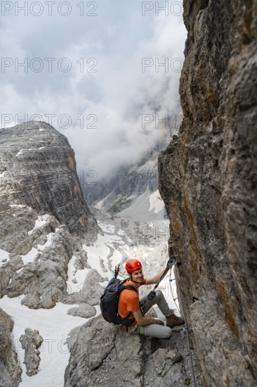 Mountaineer climbs the Via Ferrata Oliva Detassis via ferrata, view of mountain basin with steep