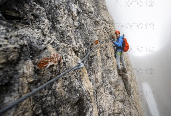 Mountaineers on a steep rock face on the Via Ferrata Oliva Detassis via ferrata in fog, steep
