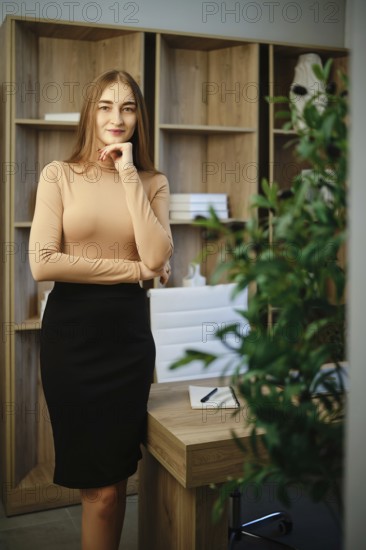 A woman stands in an office with wooden shelves behind her. She has long hair and wears a fitted