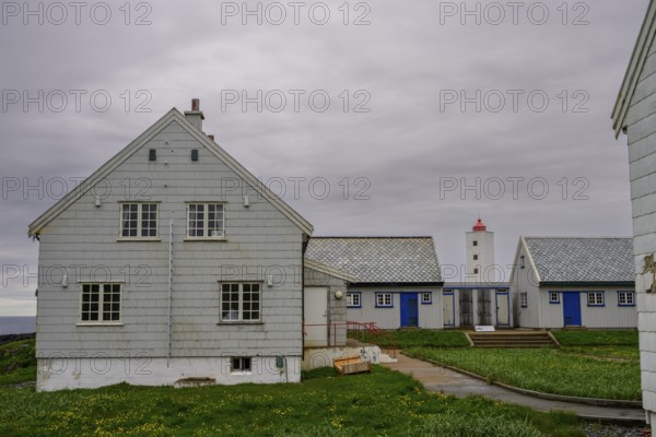 Lighthouse between blue and white houses rises under a grey sky Kjølnes Fyr, small windows and