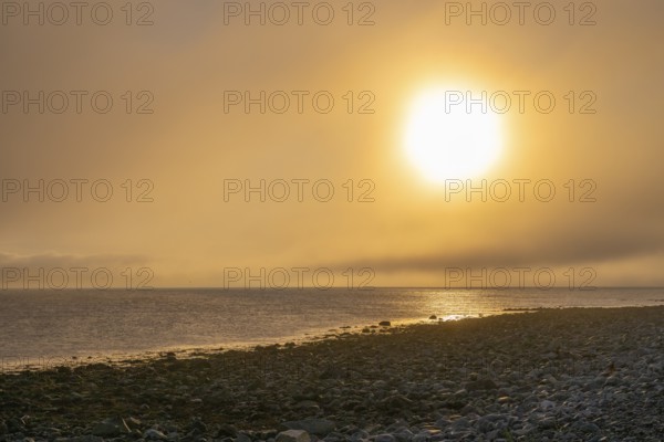 Dramatic sunset over a rocky stretch of coast with soft light, golden sky reflected in the sea,