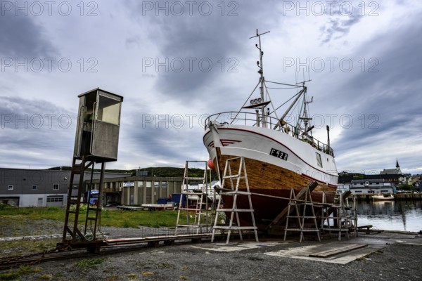 A large boat fishing trawler fishing vessel on a dry dock is positioned against a cloudy sky in the
