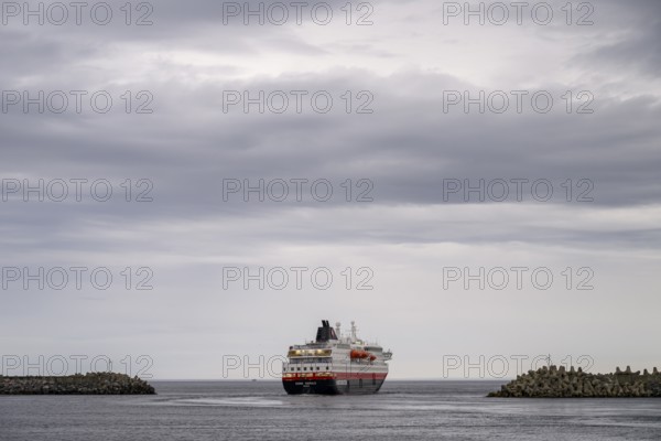 The Hurtigrouten Hurtigruten ship Kong Harald sails from Berlevag harbour, on the horizon with a