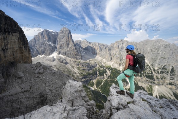 Female mountaineer on a rock in front of picturesque mountain landscape with rocky peaks, Via