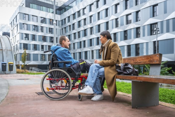 Young man living with a disability sitting in a wheelchair and having a joyful conversation with a