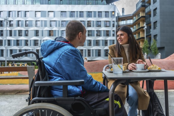 Man with disability in wheelchair talking with female friend while having coffee and pastry at an