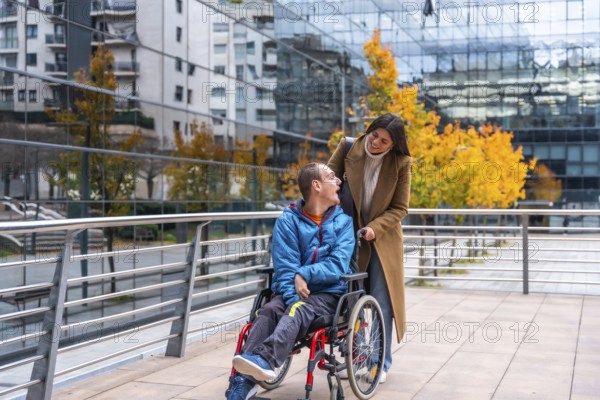 Caregiver pushing an adult man in a wheelchair on a modern city street, both individuals smiling