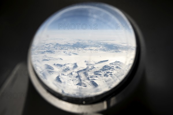 View from an airplane window of snowy arctic mountain landscape with glaciers, aerial view,