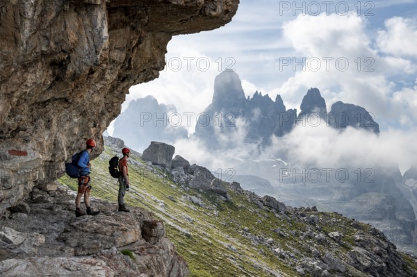 Two mountaineers on a path in front of a picturesque mountain landscape with rocky peaks, Via