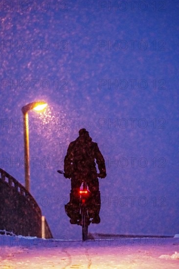 Winter weather, blowing snow, person with e-bike, bicycle on snowy bridge, footpath bridge, steep
