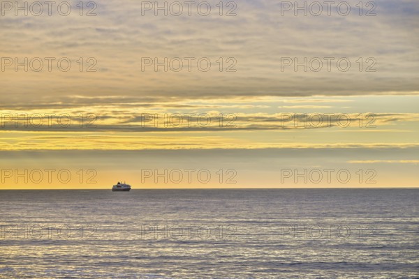 A Hurtigrute ship on the wide Barents Sea at sunset midnight sun, yellowish clouds and calm seas,