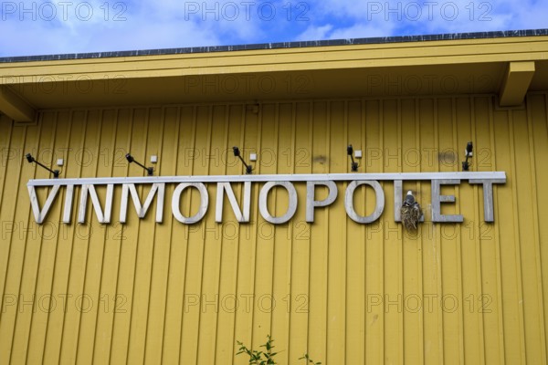 Yellow building of the Norwegian state wine monopoly with sign and floodlights and a breeding