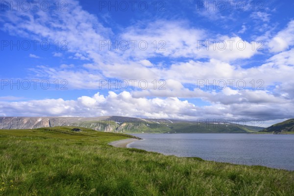 Green meadows on the banks of Syltefjord with clouds in the blue sky, landscape with a lake and