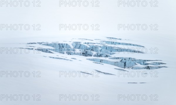 Smooth white snowy area on the glacier broken by crevasses with blue rugged glacial ice, detail,