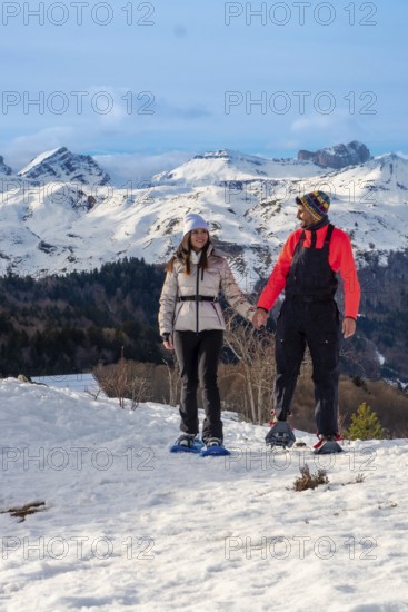 Young couple hand in hand snowshoeing on a sunny mountain trail, surrounded by vast snow capped