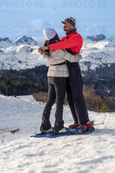 Happy couple embracing each other while snowshoeing on a snowy mountain landscape, enjoying a